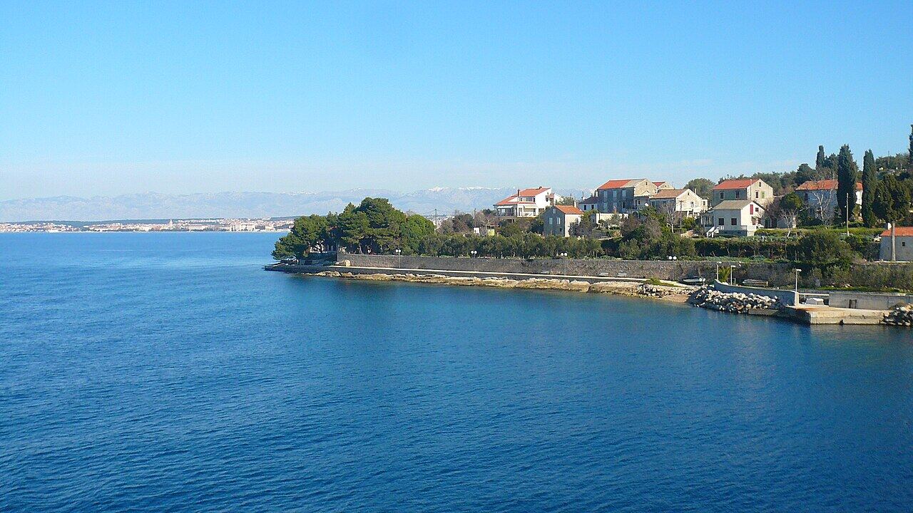 Stone houses along the shore seen from the ferry, with the mainland mountains behind
